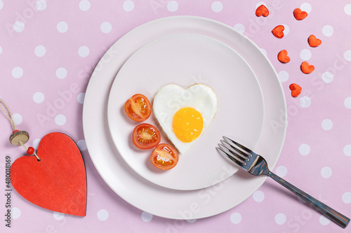 Fried eggs in the shape of a heart on a white plate and tomatoes for a healthy breakfast. The concept of Valentine's Day. Top view.
