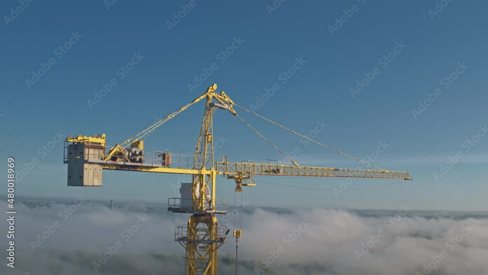 Construction site. Building new city development. Aerial flight around industrial high tower crane. Incomplete buildings. Cityscape. Inspiring scene.