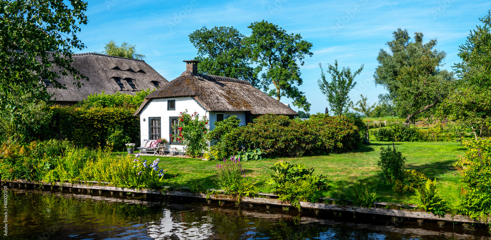 Peaceful rural landscape of Giethoorn village, the Netherlands. House with beautiful flowers in small typical village. Landscape view of houses with canals and rustic thatched roof houses.