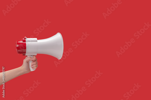 Megaphone in woman hands on a red background.