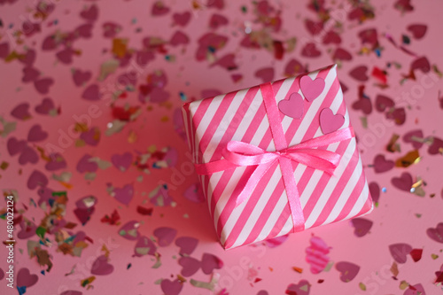 Gift box with hearts among colored confetti on a pink background for a beloved woman for Valentine's Day. Happiness to give and receive presents on holidays. 