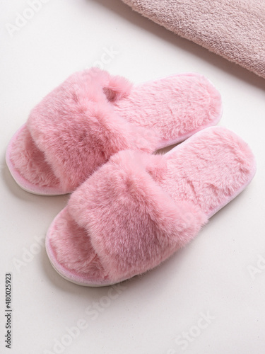 Pink women's home slippers and towel on light background. Comfortable shoes for home
