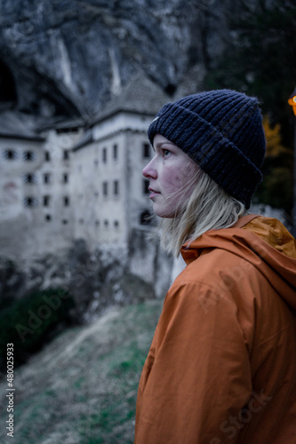Model with hat and yellow jacket in the winter in front of predjama castle, Slovenia