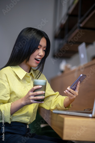 Pretty young asian woman in yellow shirt working on a laptop
