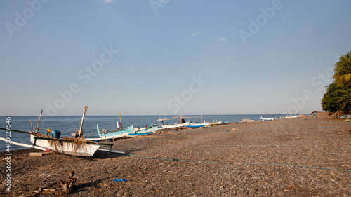 Fishing boats on the beach of Bali island. Sea and black volcanic sand.