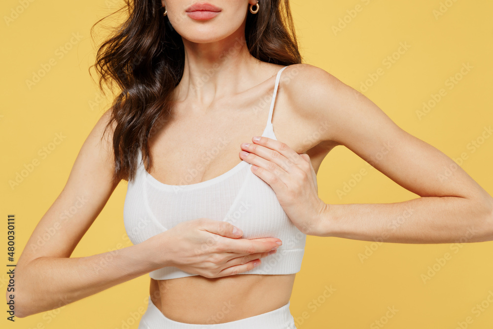 Cropped image of young caucasian woman 20s in white brassiere underwear put  hand on chest breast cancer early diagnostic therapy treatment isolated on  on plain yellow color background studio portrait. Stock Photo
