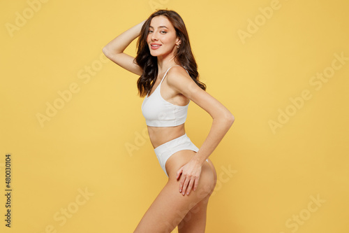 Side profile view sexy satisfied attractive young brunette caucasian woman 20s wear white underwear with perfect fit body standing posing hold head isolated on plain yellow color background studio