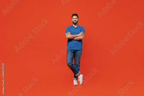 Full body young smiling confident calm happy european attractive man 20s in basic blue t-shirt hold hands crossed folded isolated on plain orange background studio portrait. People lifestyle concept