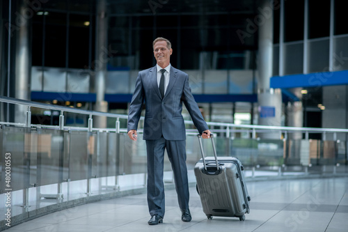 Smiling entrepreneur with his baggage walking along the airport terminal