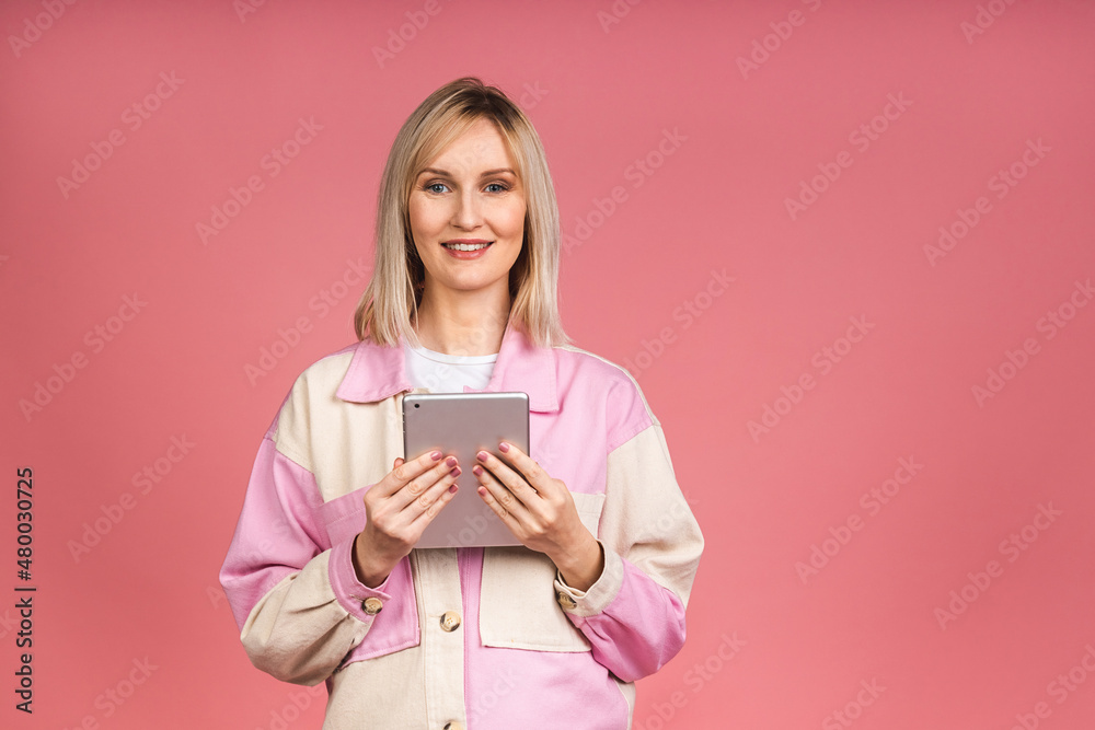 A beautiful smiling female with blond hair uses a tablet computer for education or business charting work. Smiling positive girl using modern technologies isolated over pink background. A beautiful smiling female with blond hair uses a tablet computer for education or business charting work. Smiling positive girl using modern technologies isolated over pink background.
