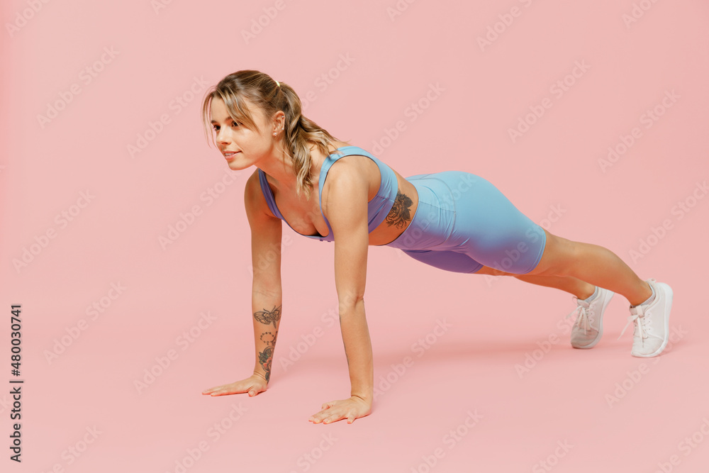 Full body young athletic fitness trainer instructor woman wear blue tracksuit spend time in home gym training doing side plank exercise pilates isolated on plain pink background Workout sport concept Full body young athletic fitness trainer instructor woman wear blue tracksuit spend time in home gym training doing side plank exercise pilates isolated on plain pink background Workout sport concept