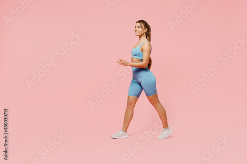 Full body fun young strong sporty athletic fitness trainer instructor woman wear blue tracksuit spend time in home gym walk going isolated on pastel plain light pink background. Workout sport concept.