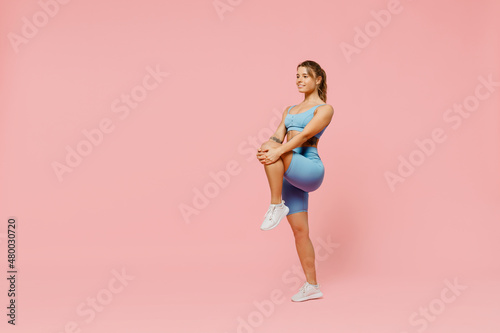 Full size young sporty athletic fitness trainer woman wear blue tracksuit spend time in home gym train do stretch legs exercise isolated on pastel plain light pink background. Workout sport concept.