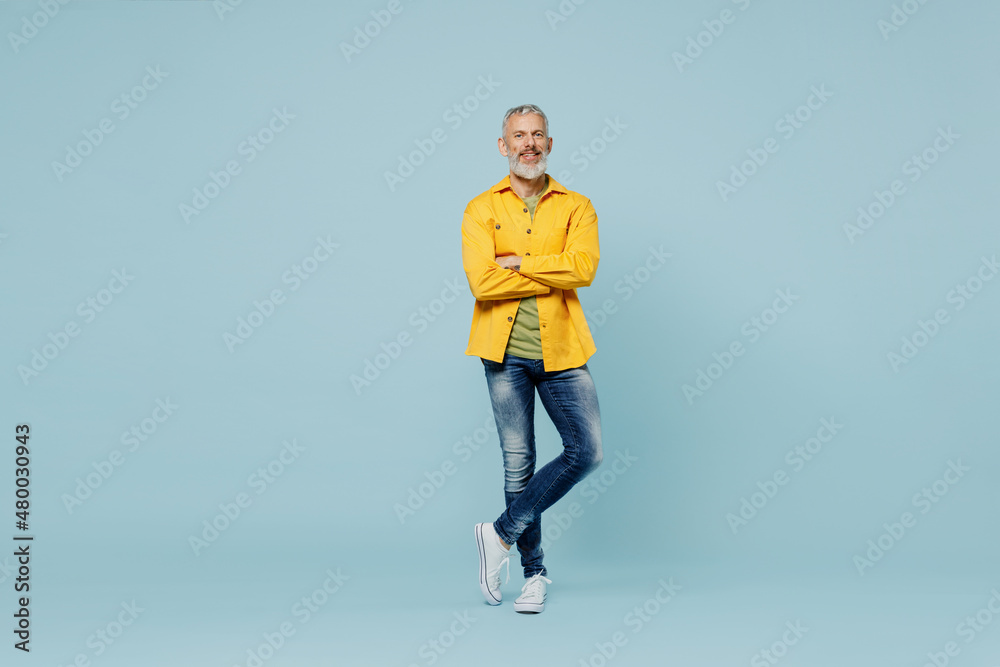 Full body elderly gray-haired mustache bearded man 50s wear yellow shirt hold hands crossed folded look camera isolated on plain pastel light blue background studio portrait. People lifestyle concept.