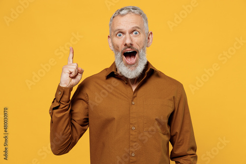 Foto Insighted smart proactive charismatic elderly gray-haired bearded man 40s years old wears brown shirt holding index finger up with great new idea isolated on plain yellow background studio portrait
