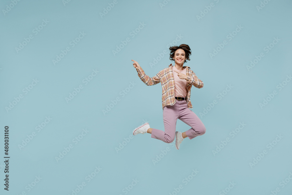 Full body young smiling happy woman 20s wearing casual brown shirt jump high point index finger aside on workspace area mock up isolated on pastel plain light blue color background studio portrait Full body young smiling happy woman 20s wearing casual brown shirt jump high point index finger aside on workspace area mock up isolated on pastel plain light blue color background studio portrait