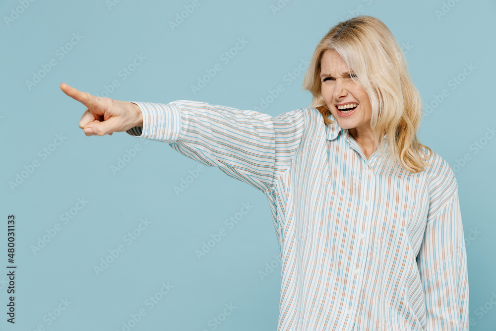 Elderly angry indignant strict caucasian woman 50s wear striped shirt point index finger aside scream isolated on plain pastel light blue color background studio portrait. People lifestyle concept. Elderly angry indignant strict caucasian woman 50s wear striped shirt point index finger aside scream isolated on plain pastel light blue color background studio portrait. People lifestyle concept.