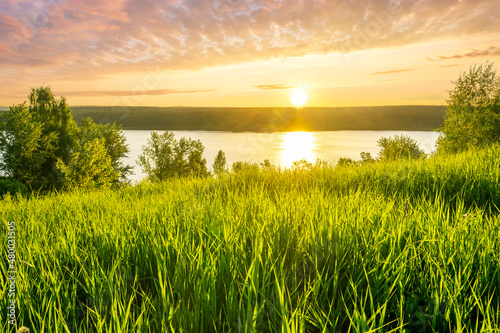 Fototapeta Naklejka Na Ścianę i Meble -  scenic view at nice landscape on a beautiful lake and colorful sunset with reflection on water with green gras on foreground and glow on a background, spring season landscape