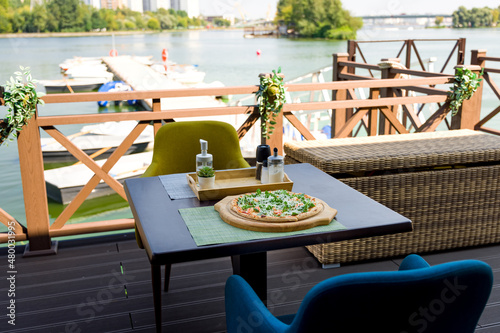 Pizza with arugula and shrimp on table near a water