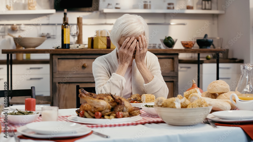 depressed woman obscuring face with hands while sitting at table served with thanksgiving dinner.