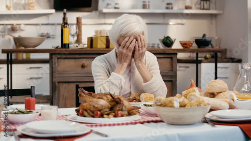 depressed woman obscuring face with hands while sitting at table served with thanksgiving dinner.