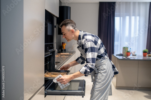 Profile of man putting baking sheet in oven