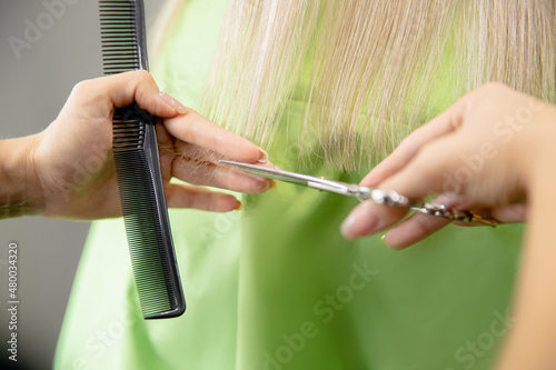 Close-up of master hairdresser shears with scissors dry ends of woman hair in salon