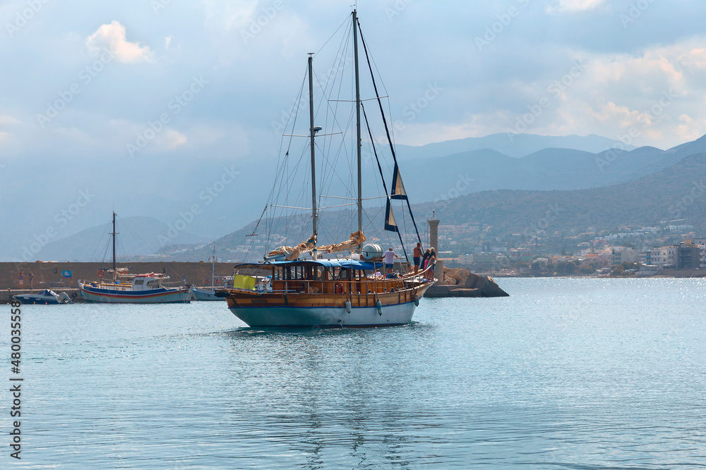 a small sailing yacht with tourists comes out of a quiet yacht into the open sea. Crete. Greece