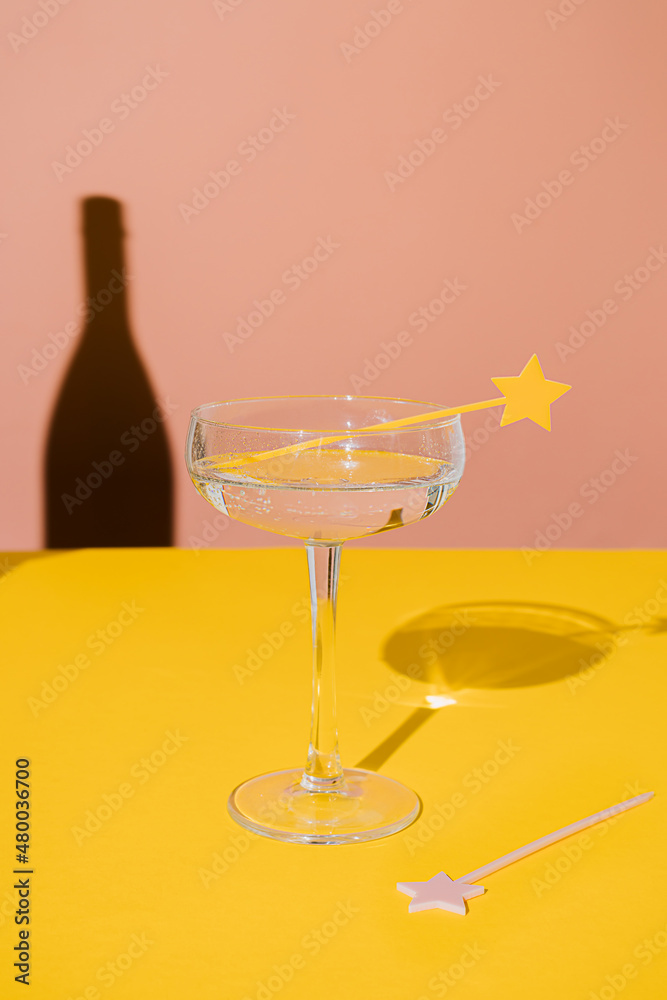 Champagne coupe glass with a star cake pick topper and a sharp champagne shadow on yellow and pink vivid background. Minimal modern still life. Party celebration concept. Luxury concept. Champagne coupe glass with a star cake pick topper and a sharp champagne shadow on yellow and pink vivid background. Minimal modern still life. Party celebration concept. Luxury concept.