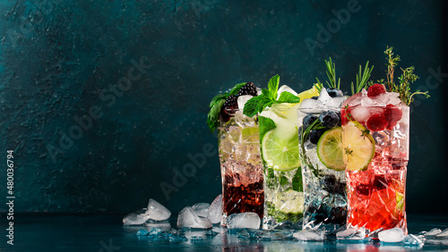 Cocktails or mocktails drinks. Classic summer refreshing long drink in highballs with berries, lime, herbs and ice on blue table background photo