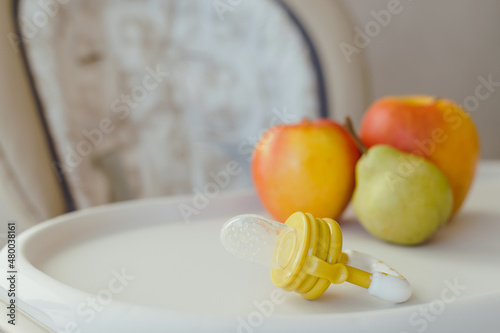 Nibbler with fresh apples and pear on light kids table, closeup. Baby feeder photo