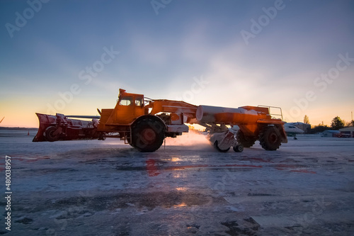 A special airfield cleaning machine cleans the snow at sunset