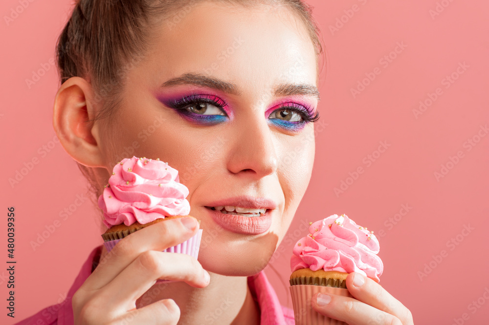 Professional makeup in pink and blue colors. Close up portrait of young girl with bright evening makeup holding cupcakes. Professional makeup in pink and blue colors. Close up portrait of young girl with bright evening makeup holding cupcakes.