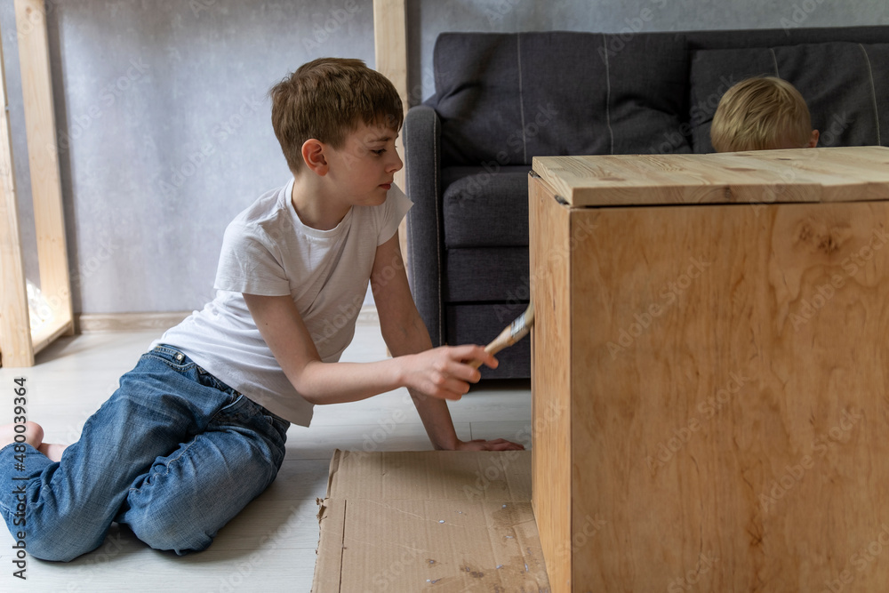 Teenage boy helps restore an old table. Child paints wooden pedestal with brush. Side view Teenage boy helps restore an old table. Child paints wooden pedestal with brush. Side view