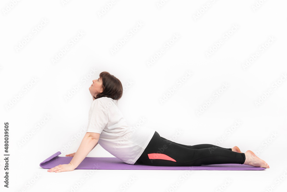 Young woman who is overweight practice yoga. Girl is trying to lose weight and goes in for sports on yoga mat. Side view. White background.