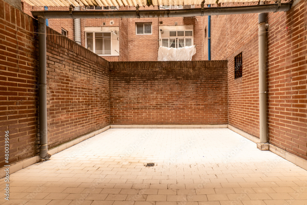 Inner courtyard on the ground floor of a residential building with covered part and clay brick walls with white porcelain floors