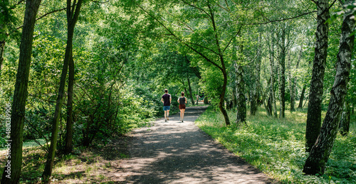 A young woman and a young man are running in the distance on a trail in a public park. 