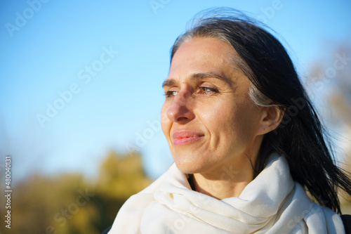 Profile side view portrait of attractive cheerful dreamy grey-haired middle-aged woman relaxing outdoors during sunny day