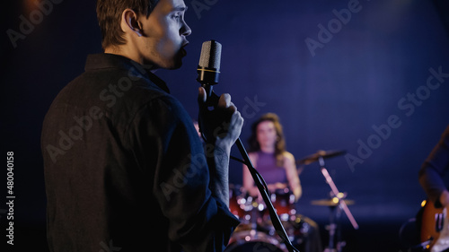 young singer singing in microphone near blurred music band.