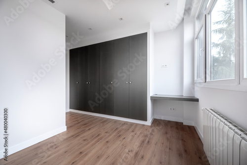Nice room with large window, pine wood floors and built-in wardrobes with gray doors with wall-mounted study table
