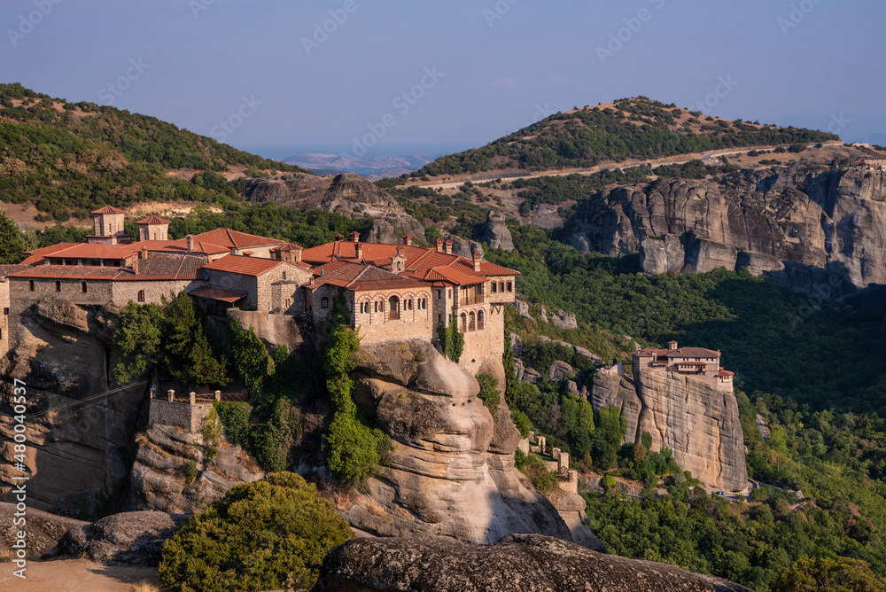 Beautiful scenic view of Orthodox Monastery of Áyios Nikólaos Anapafsás (St. Nicholas Anapafsas) on cliff, at the background of stone wall and rock formations of Meteora mountain, Greece.