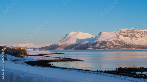 View at the island of Senja and the fjord in the Atlantic Ocean with a snowy field in the polar area and mountains covered in snow near Tromso Norway