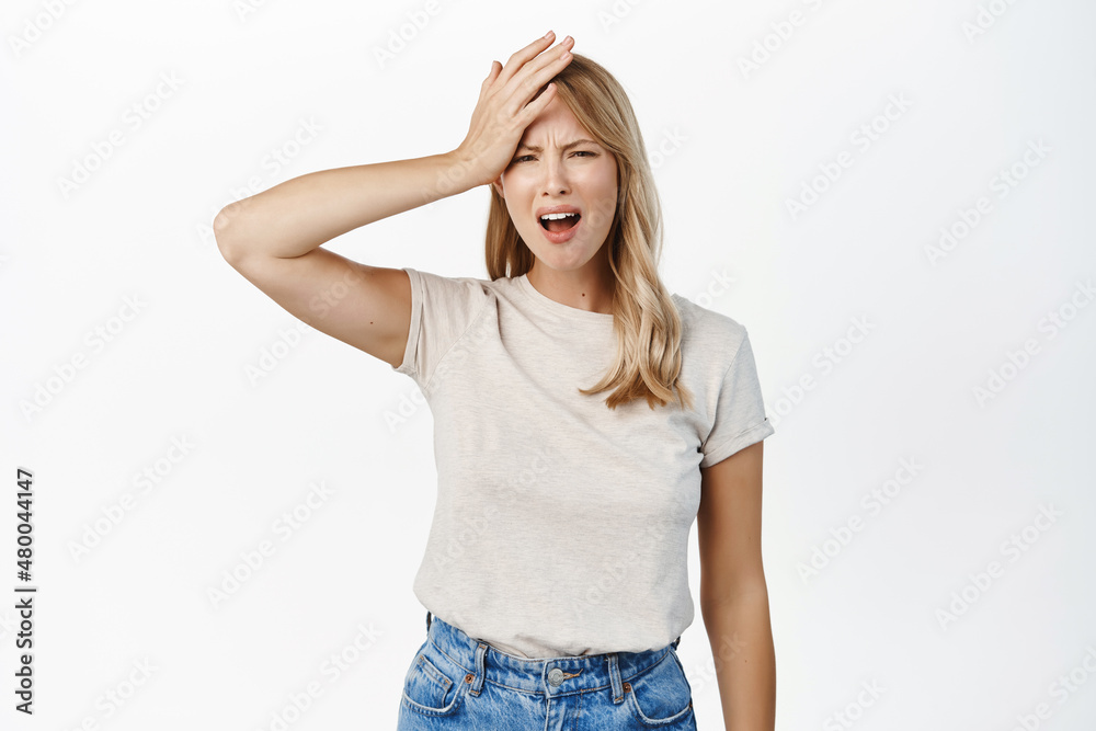 Disaster. Troubled blond girl holding hand on head and grimacing, feeling disappointed, upset by smth, standing over white background Disaster. Troubled blond girl holding hand on head and grimacing, feeling disappointed, upset by smth, standing over white background