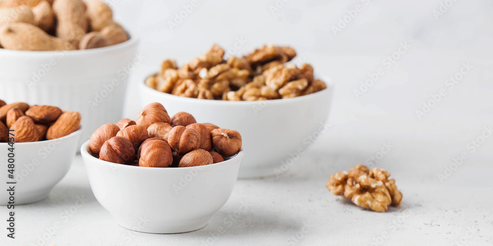 Hazelnuts and other nuts in white bowls on a white background. Banner Hazelnuts and other nuts in white bowls on a white background. Banner