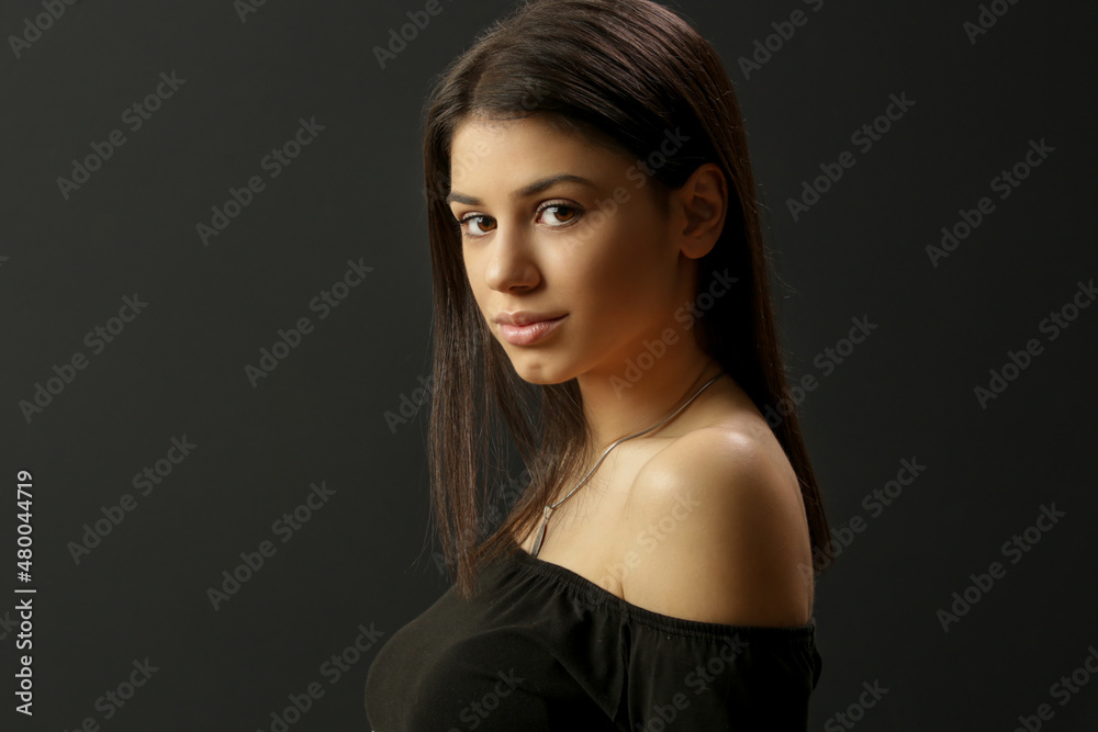 Portrait of attractive young brunette wearing cold shoulder top on black background