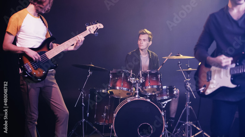 blurred guitarists and drummer performing on stage.