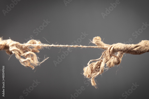 Frayed rope about to break on grey background. Risk