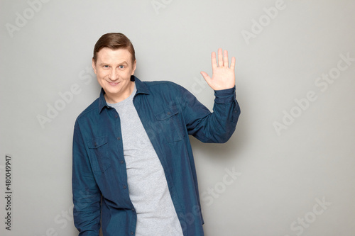 Portrait of happy friendly mature man raising hand and waving palm