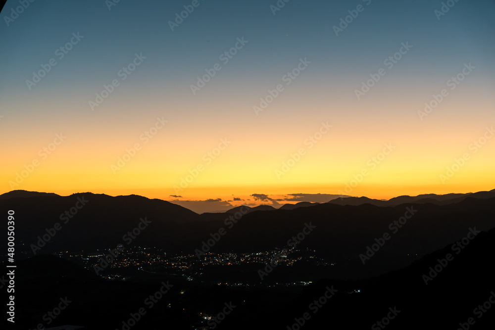 Dramatic image of a Caribbean mountain sunset high in the Dominican Republic with a snall town in the valley with street lights.