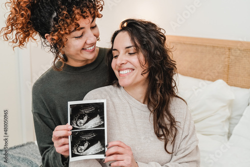 LGBT lesbian couple holding ultrasound photo scan of growing baby in pregnancy time - Focus on right woman face photo